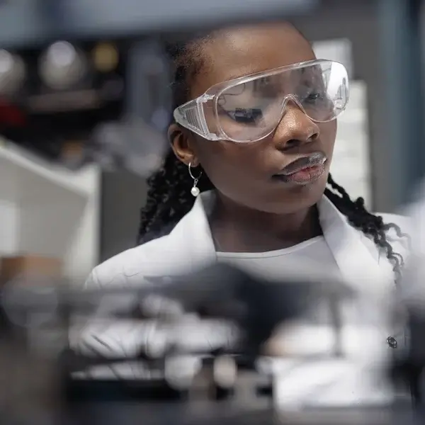 A scientist wearing safety goggles and a white lab coat focuses intently on an experiment, perhaps analyzing employee compensation or conducting salary benchmarking in a laboratory setting.
