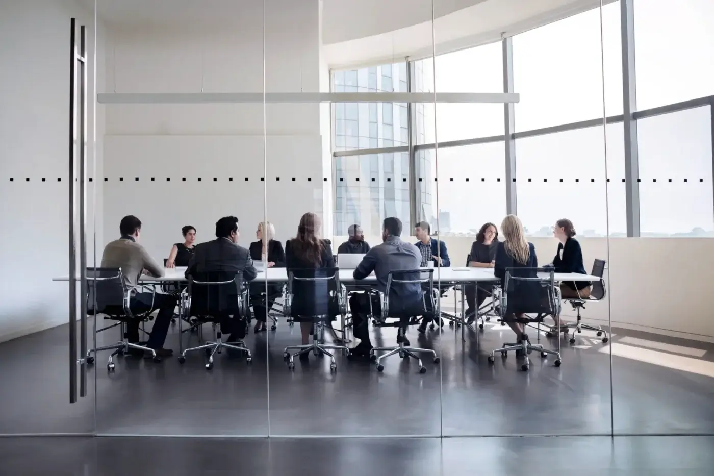 A group of people sit around a large conference table in a modern office meeting room with floor-to-ceiling windows and glass walls, discussing employee compensation strategies and salary comparison data.